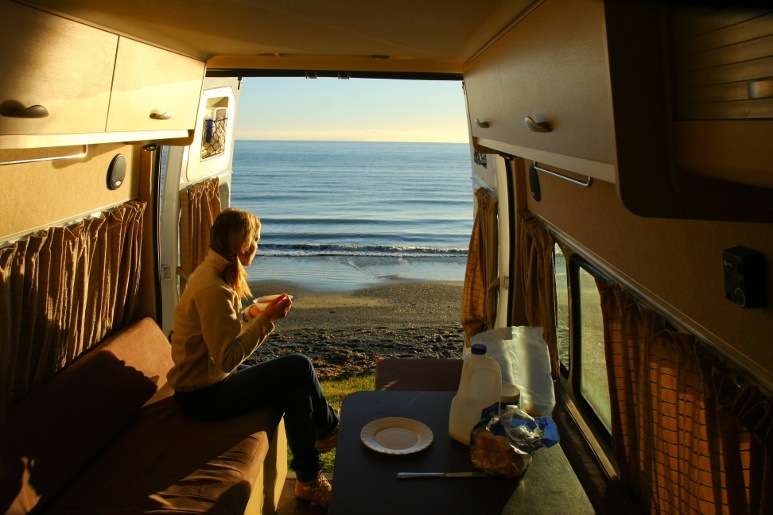 Woman having coffee in RV camped by the seaside