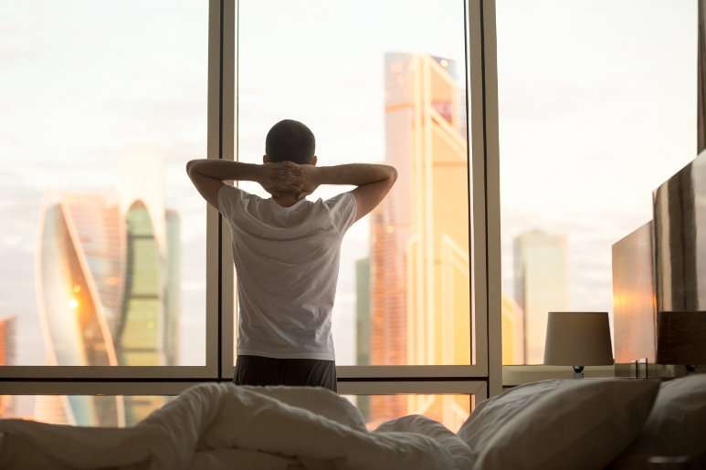 Successful man looking out the window in the morning after a good night's sleep