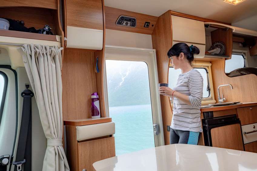 Woman in the interior of a RV with a cup of coffee looking at nature.