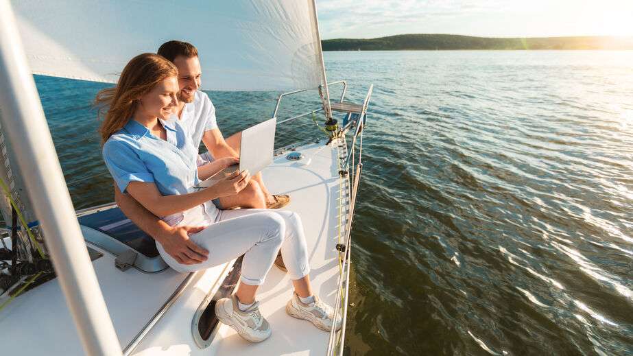 Happy couple living on a boat and using their laptop to work.