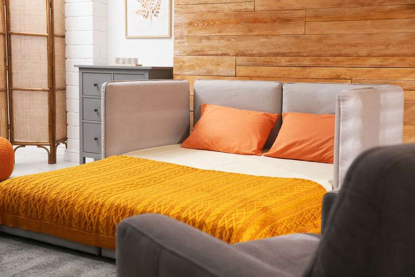 Sofa unfolded into bed near wooden wall in room.