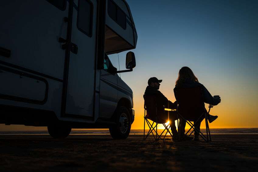 Caucasian Couple Relaxing Next to Their RV Motorhome on the Pismo Beach During Scenic Sunset.